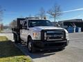 A 2011 Ford F-350 SD with a flatbed and orange warning lights on the roof parked on a street