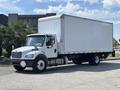 A 2015 Freightliner M2 106 box truck with a white cargo area and a black chassis parked with a front view showcasing the driver's side and front features
