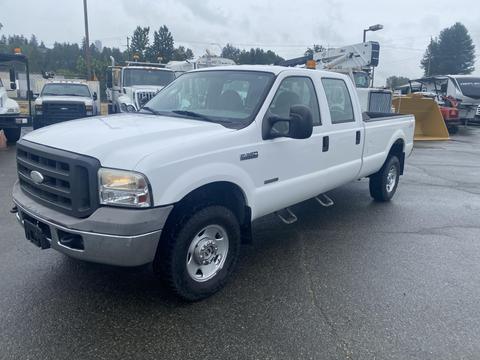 A white 2005 Ford F-350 SD with a crew cab and a flatbed is parked, showcasing its sturdy build and off-road tires