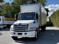 A 2021 Hino 338 truck with a white cab and a silver box trailer parked with trees in the background
