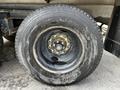 Close-up of a tire mounted on a steel rim featuring multiple lug nuts, showing signs of wear and a rough surface on the tire tread