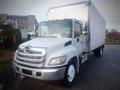 A 2013 Hino 308 box truck with a white exterior and chrome grille parked in a lot with a large cargo area behind the cab