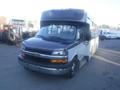 A 2016 Chevrolet Express bus with a dark front, yellow headlights, and large windows on the side is parked with no other vehicles in the foreground