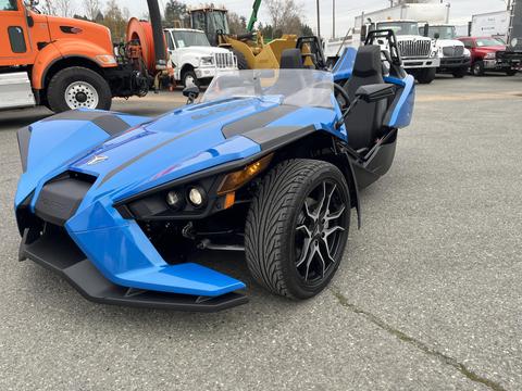 A blue 2020 Polaris Slingshot with a sleek design featuring two front wheels and a single rear wheel is parked with its canopy partly open