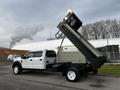 A 2021 Ford F-550 with a dump bed raised, showcasing its heavy-duty design and two-tone white and black exterior