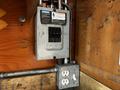 A gray electrical panel featuring circuit breakers and a power outlet mounted on a wooden wall