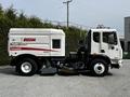 A white 2012 Autocar Xpert street sweeper with a brush attachment and a large sealed compartment on the side for collecting debris