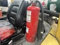 A red fire extinguisher mounted beside a black seat in a vehicle