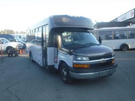 A 2016 Chevrolet Express bus with a black front and white body parked with its door open and a slight angle towards the viewer