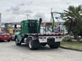 A green 2013 Kenworth T370 truck with a flatbed and black railings is parked, showcasing its distinctive cab design and rear features
