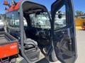 A 2014 Kubota X1100C utility vehicle with a red and black exterior featuring an open cabin door and a spacious driver's seat and dashboard displayed inside