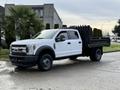 A 2017 Ford F-450 Super Duty pickup truck with a flatbed and black railing on the back parked on a street