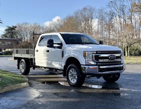 A white 2020 Ford F-350 truck with a flatbed and chrome grille parked on a wet street
