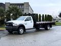A white 2018 RAM 5500 flatbed truck with a black bed and black side rails parked on a street surrounded by greenery