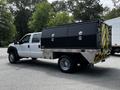 A 2016 Ford F-550 with a dual cab design and a black utility box attached to the flatbed featuring reflective stripes and multiple storage compartments