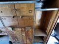 A wooden storage cabinet with multiple drawers and compartments featuring brass handles and an open shelf space on the right