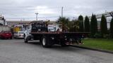 A white 2008 Ford F-750 flatbed truck with a wooden flatbed and a small palm tree on it