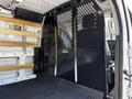 Interior of a 2023 Ford Transit showing a partition with metal mesh and wooden shelves against the side walls of the cargo area