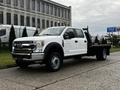 A white 2021 Ford F-550 truck with a flatbed and dual rear wheels parked on a concrete surface