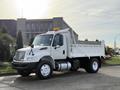 A white 2015 International DuraStar 4300 dump truck with an open bed and front warning light