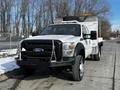 A 2011 Ford F-450 Super Duty truck with a white body and black details featuring a front bumper guard and a flatbed with tools on the back
