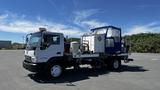 A 2006 Ford LCF 550 truck with a modified flatbed carrying a blue and white enclosed structure and additional equipment mounted on the chassis