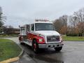 A 2001 Freightliner FL80 fire truck with a red and white color scheme features emergency lights on top and a ladder on the side