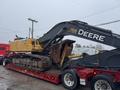 A yellow 2014 John Deere 350G excavator with a large digging bucket sits on a red flatbed truck trailer