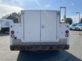 A white 2015 Ford F-450 SD facing the viewer with a large flatbed and doors at the rear showcasing a simple industrial design and faded paint on the lower portion