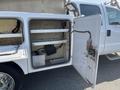 A white 2015 Ford F-450 SD with an open utility compartment revealing metal shelves and wiring inside