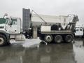 A 2023 Mack Granite truck with a concrete mixer attachment facing right with a gray and white color scheme and multiple axles