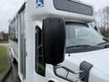 A 2013 Chevrolet Express bus with a black side mirror and accessibility symbols on the front windshield