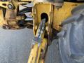 Close-up of a yellow 2007 Komatsu WB156PS-5 tractor showing the hydraulic linkage and chain mechanism attached to a large tire