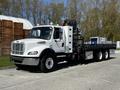 A 2012 Freightliner M2 112 truck with a flatbed and mounted crane, featuring a white exterior and a spacious cabin with multiple lights on the roof