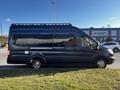 A 2017 Ford Transit van with a long body and roof rack parked on a grassy area with silver rims and black exterior