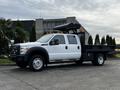 A 2015 Ford F-550 with a flatbed and dump feature in a white exterior paint and a dual cab configuration featuring black wheels and safety lights on the roof