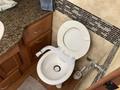 A white toilet inside a motorhome bathroom with a tiled wall and wooden cabinetry