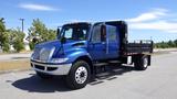 A blue 2012 International DuraStar 4300 truck with a flatbed and step ladder on the side parked on a paved surface