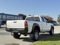 A white 2015 Toyota Tacoma with a standard cab and a lift kit parked on a driveway showcasing its rear and profile design