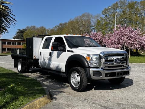 A white 2016 Ford F-550 truck with a flatbed and toolbox in the rear, featuring a chrome grille and orange lights on top
