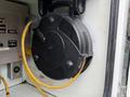 A black retractable electrical cable reel mounted on a wall with a yellow power cord extending from it