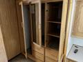 A wooden wardrobe with multiple doors and shelves featuring a light wood finish and brass handles
