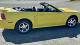 A bright yellow 2003 Ford Mustang convertible with a black interior and chrome wheels parked with the top down