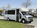 A white 2010 Ford Econoline shuttle bus with large windows and an open side door parked on a street