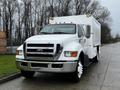 A 2013 Ford F-650 with a white cargo box and chrome accents parked on a wet road, features large wheels and a prominent front grille