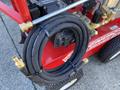 A red 2024 Magnum 4000 Hot Water Pressure Washer with a coiled black hose attached to the side featuring brass fittings and a control panel