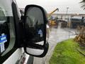 A 2018 RAM Promaster with a side mirror reflecting raindrops and a blurred background of machinery