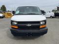 A 2013 Chevrolet Express van is shown from the front with a white exterior and black grille featuring the Chevrolet bowtie emblem. The headlights are rectangular and highlighted with orange trim