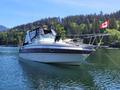 A white 1991 Larson Mirado boat with a black canopy and a Canadian flag on the stern anchored in calm water