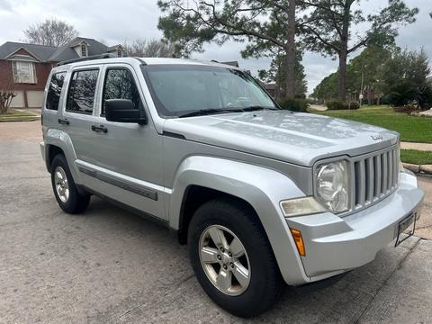 A silver 2013 Jeep Liberty Sport parked on a street showcasing its angular design and five-spoke alloy wheels
